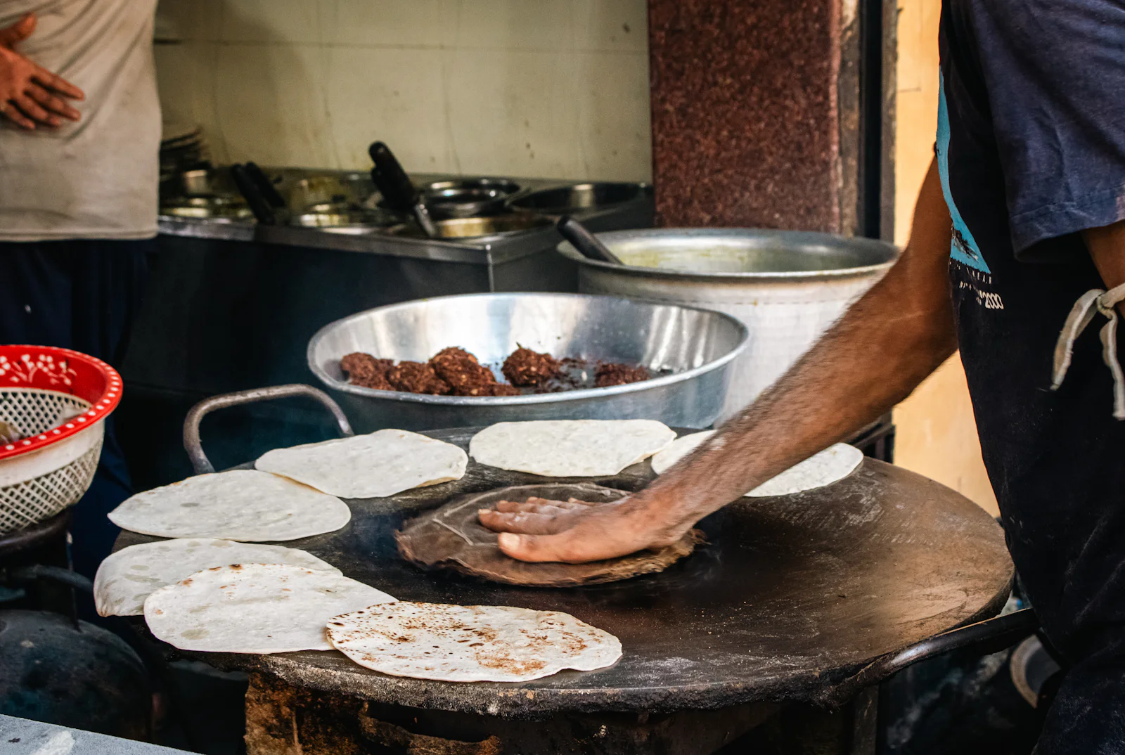 Roti dough being stretched on the round hot plate