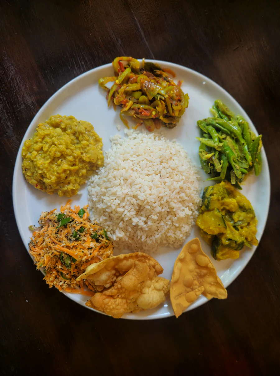 A plate of rice with dhal, green beans, carrot sambol, potato curry and papadum