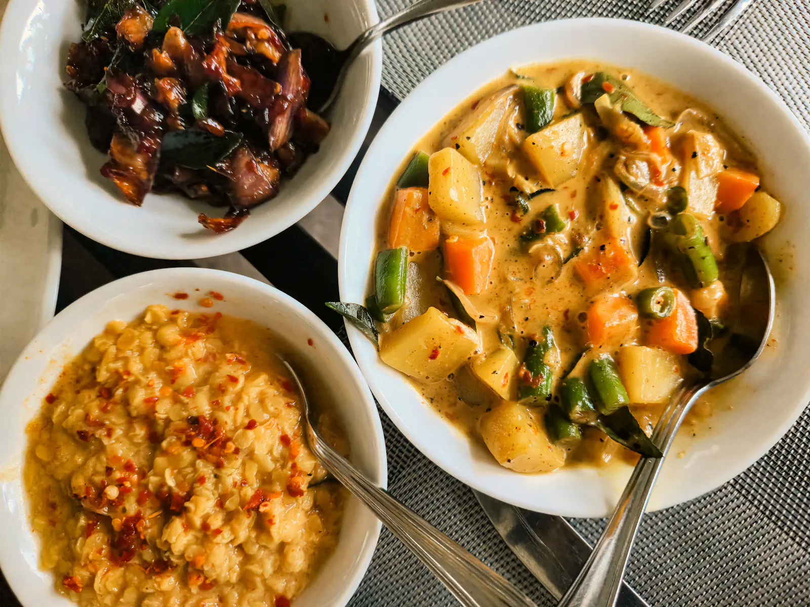 Bowls of devilled chicken, dhal and vegetable curry with spoons